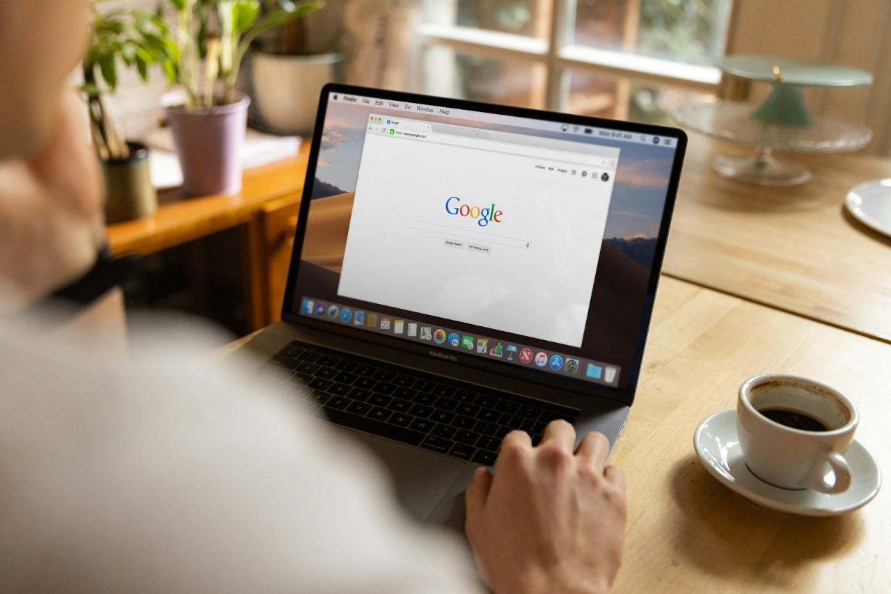 Person searching Google on a laptop beside a cup of coffee