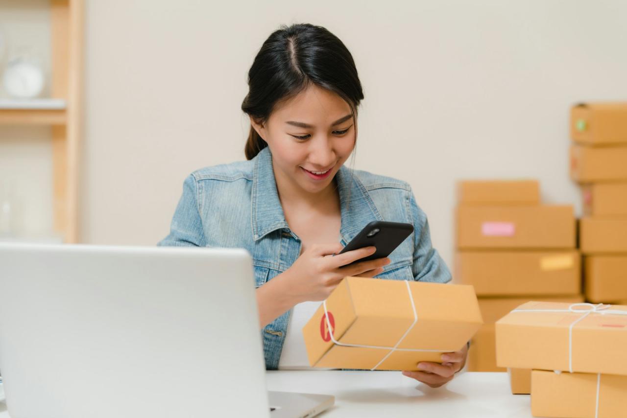 Online shop owner checking an order on her phone beside parcels